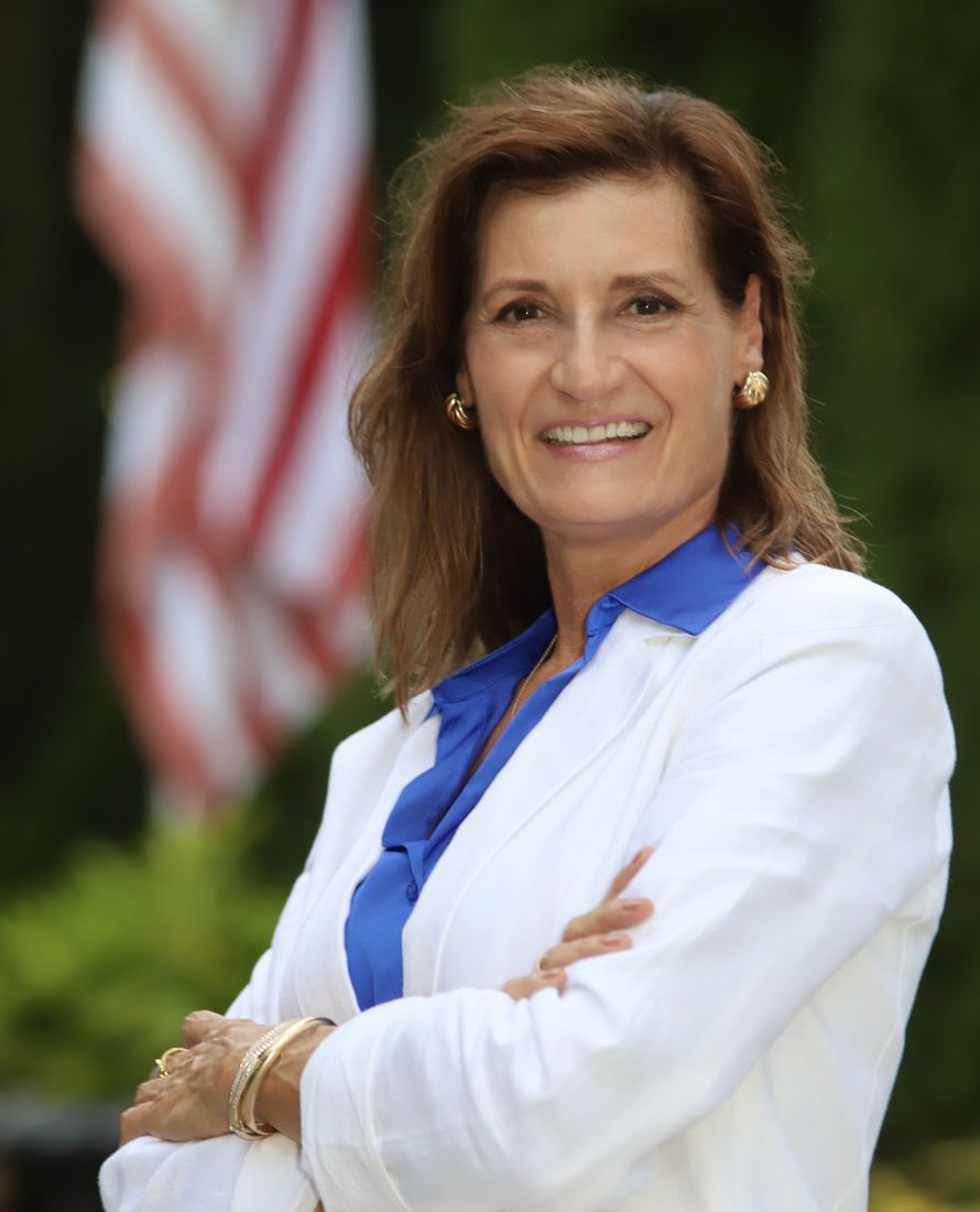 Kimberly J. Rimmer in a white blazer with an American flag behind her